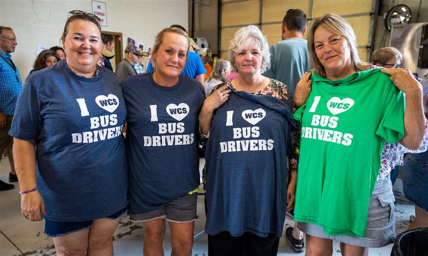 Four bus drivers hold up t-shirts that read \